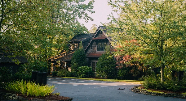 The exterior of a multi-story cabin-style building with dark wood shingles and large windows, nestled among lush green trees and a paved parking area.